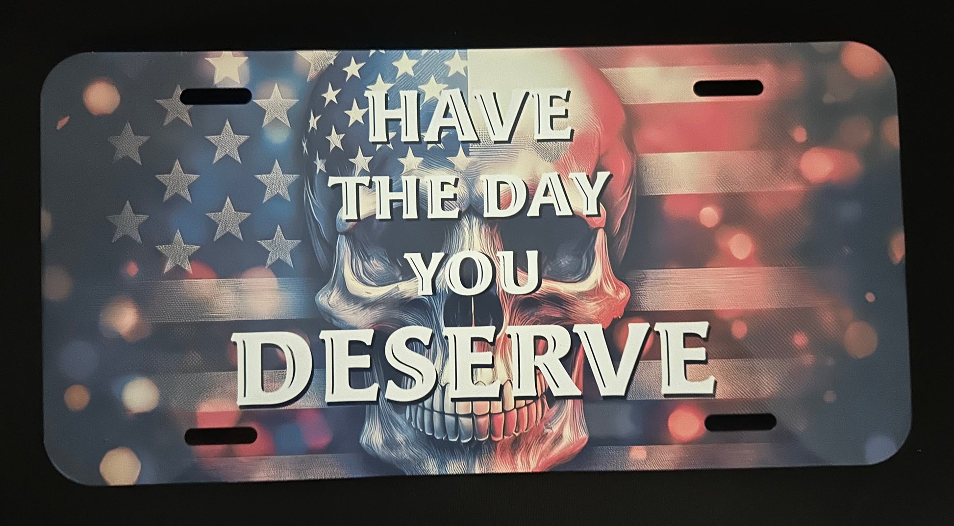 License plate with skull design and text 'Have the day you deserve' on an American flag background.