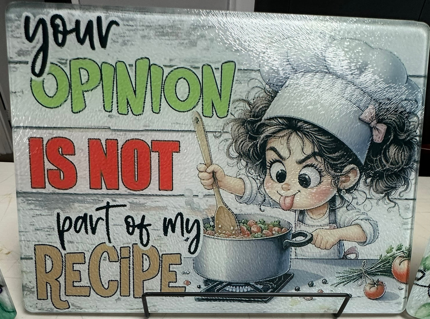 Decorative sign with a cartoon chef and text 'your opinion is not part of my recipe' on a wooden background.